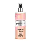 Bruno Banani Radiant Woman 250ml-es női testpermet és hajpermet hengeres, átlátszó flakonja ezüst porlasztófejjel, barackszínű folyadékkal és rózsaszín mintás felirattal.